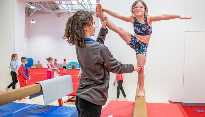 girl balancing on beam with coach assistance