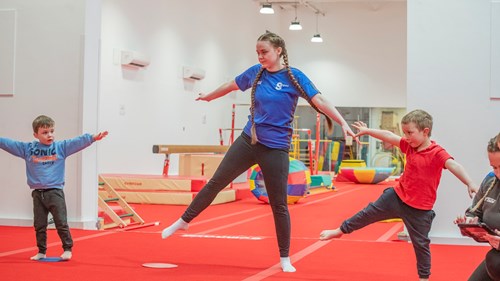 A gymnastics instructor showing two children how to do a balance during a session