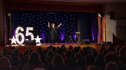 The performer Elaine C Smith stands on a raised stage in front of a packed audience