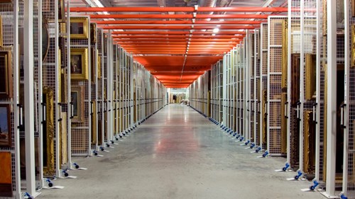 A view down a corridor in the vast painting store at Glasgow Museums Resource Centre with racks of paintings either side